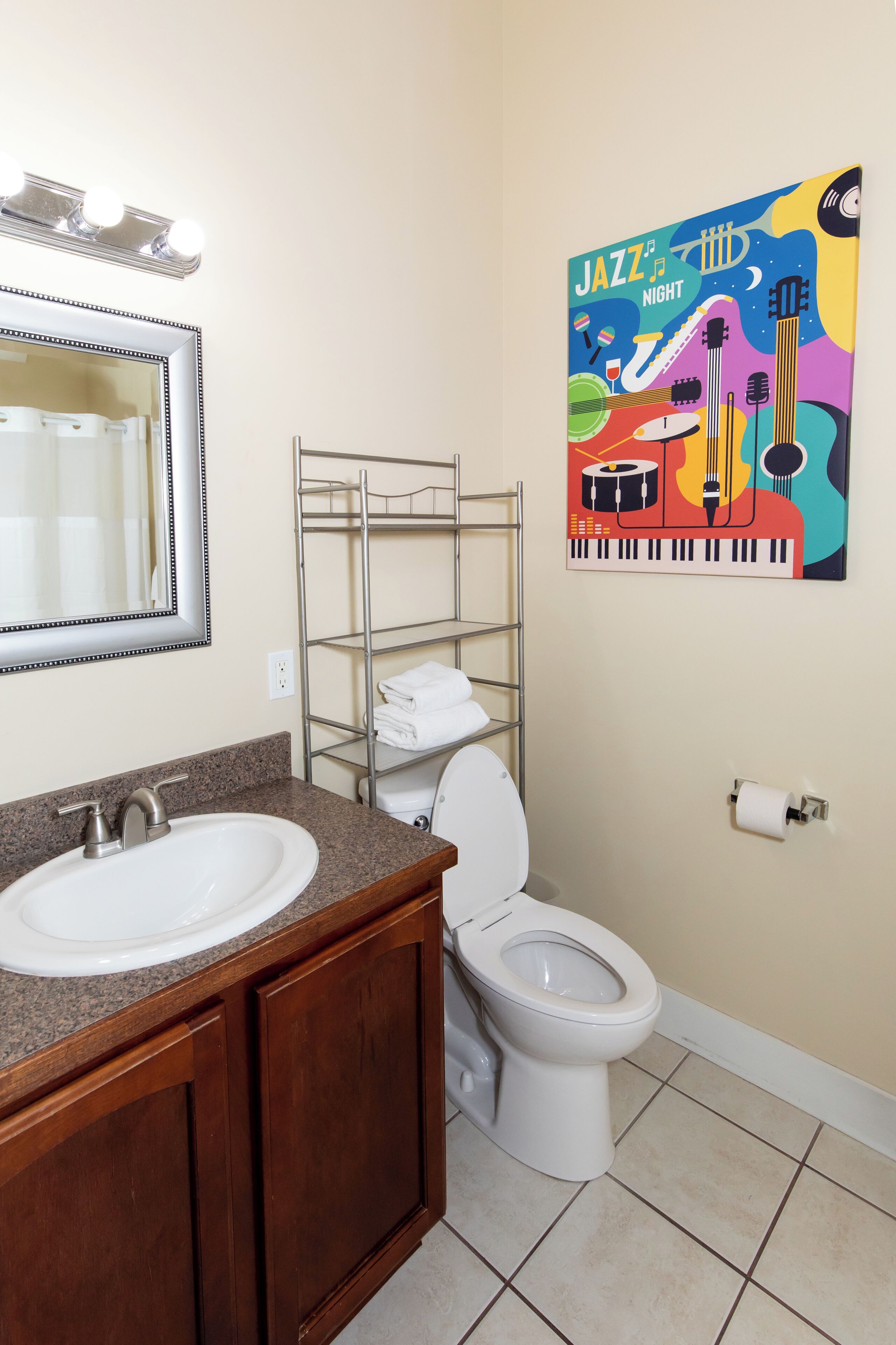 A bathroom with a sink, mirror, toilet, and a shelf with towels.