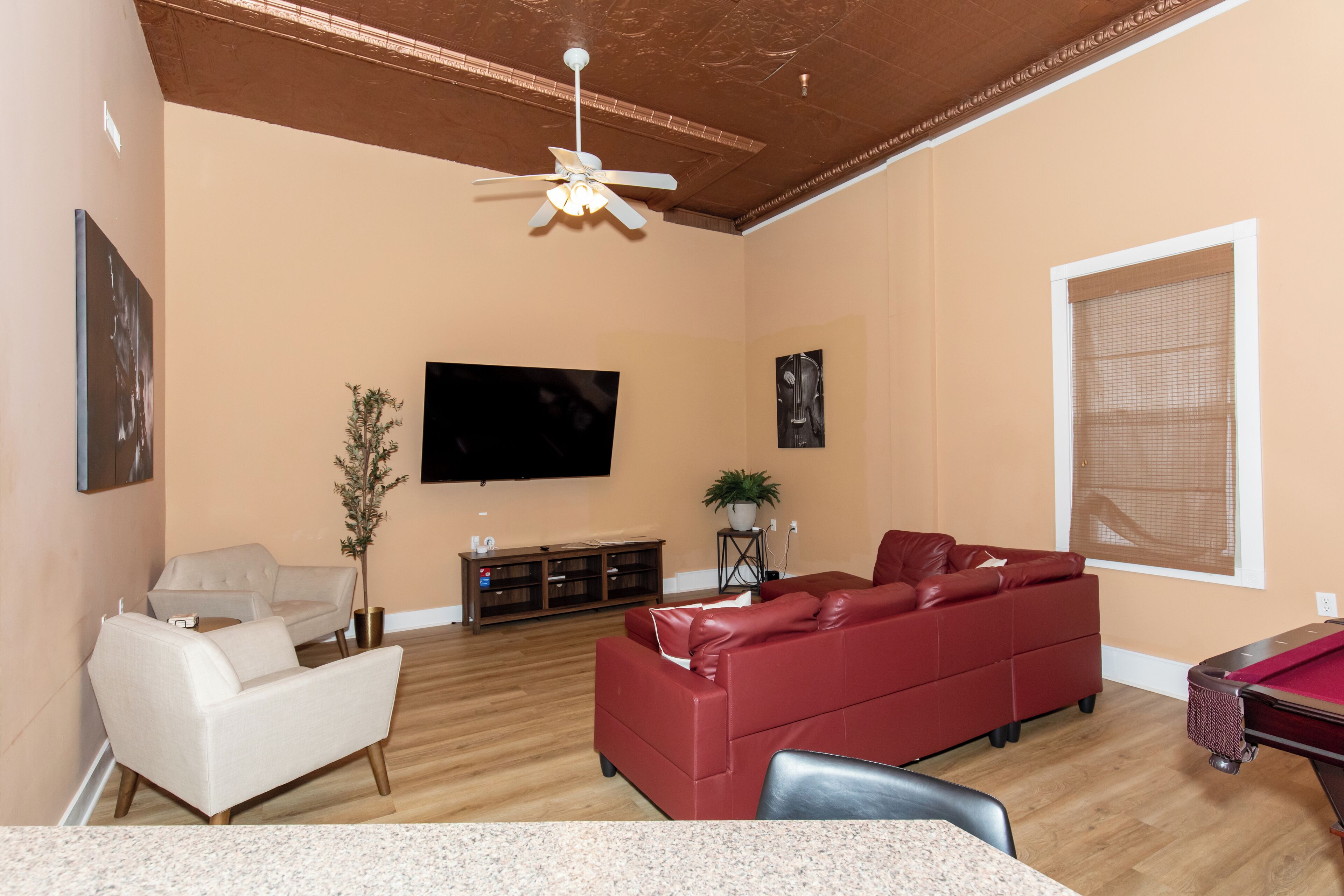 A living room with a red sofa, a beige sofa, a flat-screen TV, a ceiling fan, and a pool table.