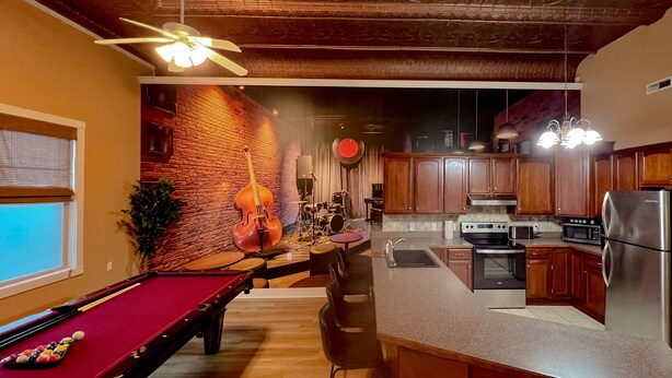 Una cocina moderna con una isla central, electrodomésticos integrados y una mesa de billar en la habitación contigua.