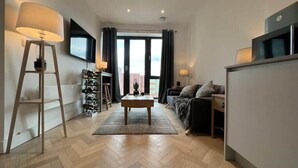 A modern living room with a sofa, coffee table, TV, and a view of the city. - 1 Bed w/ Parking| Ideal for work stays By Tempstay (Slough)