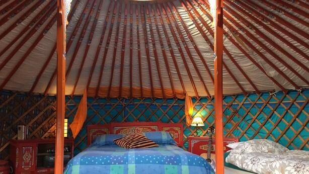 Eine traditionelle Jurte mit einem Bett in der Mitte, einem kleinen Tisch und einer Lampe.