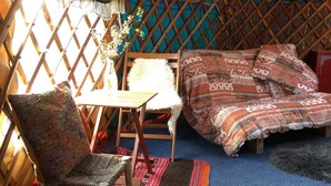 Ein gemütliches Interieur mit einem hölzernen Bett, einem gewebten Sessel, einem kleinen Tisch und einer dekorativen Wandgabe.