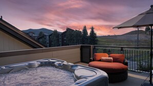 Un bain à remous sur un balcon offrant une vue sur les montagnes et un coucher de soleil.