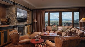 Un salon spacieux, doté de meubles en cuir, d’une cheminée en pierre, d’un grand téléviseur et d’un balcon offrant une vue panoramique.