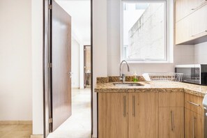 Une cuisine moderne avec des meubles en bois, un plan de travail en granit, un four à micro-ondes encastré et une fenêtre au-dessus de l’évier.