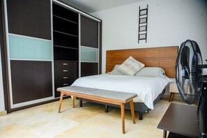 A bedroom with a bed, a bench, a wardrobe, and a fan.