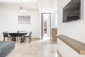Un espace de vie moderne comprenant un coin repas, un téléviseur fixé au mur et une vue sur la cuisine.