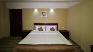 A hotel room with a large bed, two bedside tables, a door, and a framed picture on the wall. - BakurianiPearl (Borjomi)