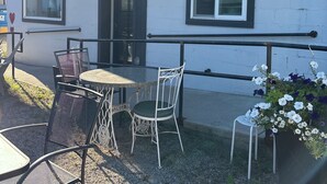 An outdoor seating area with a table and chairs, a small garden with flowers, and a building with a white exterior and black trim. - Boutique Downtown Suite | Walk to Shops & Cafés | Sleeps 6 (Armstrong)