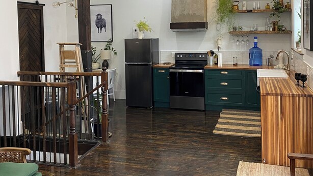 A modern kitchen with dark wood flooring, a dining area with a wooden bench, and a staircase leading to another level. - Boutique Downtown Suite | Walk to Shops & Cafés | Sleeps 6 (Armstrong)