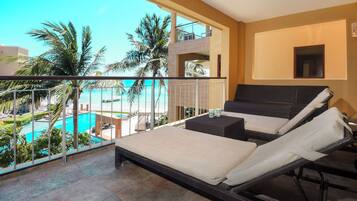 Un balcon avec vue sur la piscine, deux chaises longues, une petite table et un téléviseur.