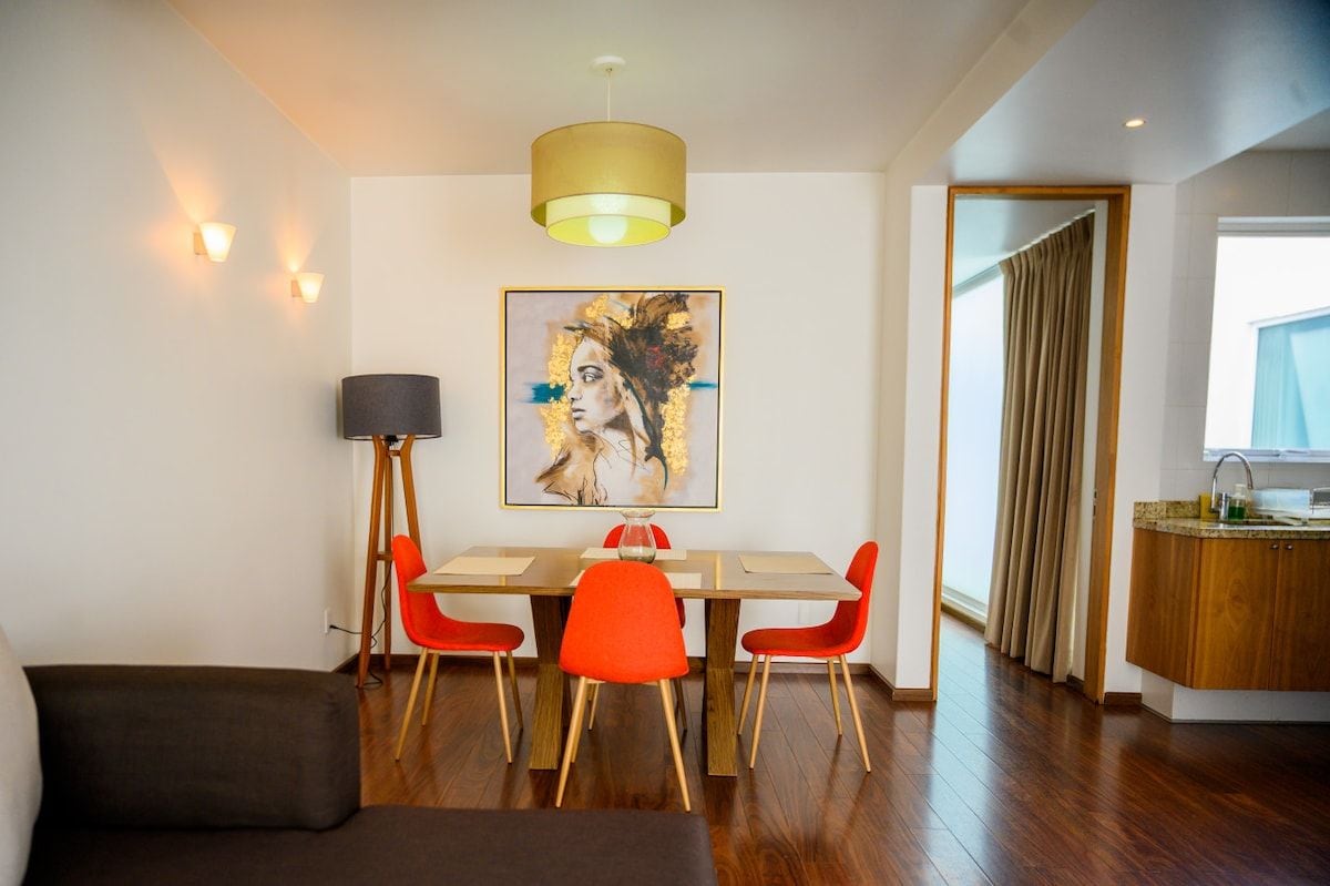 A modern dining area with a table, chairs, and a painting on the wall.
