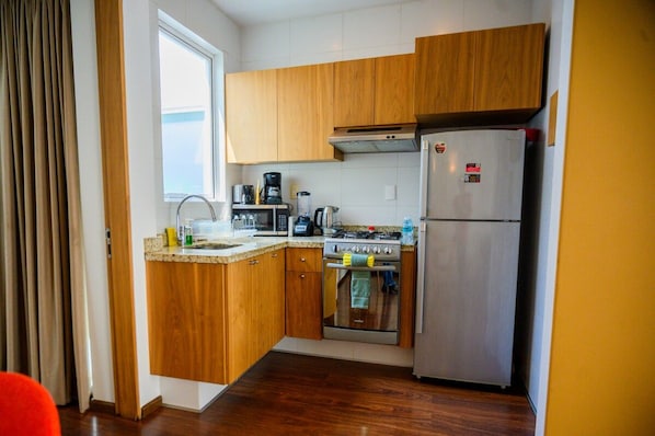 A compact kitchen with wooden cabinets, a stainless steel refrigerator, a stove, and a microwave.