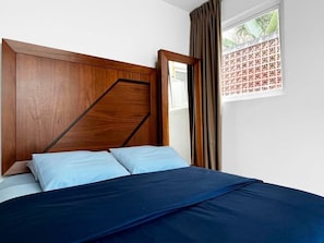 A bedroom with a wooden headboard, a bed with blue bedding, and a window with a view of greenery.