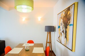 A dining area with a wooden table, orange chairs, a glass vase, and a painting on the wall.