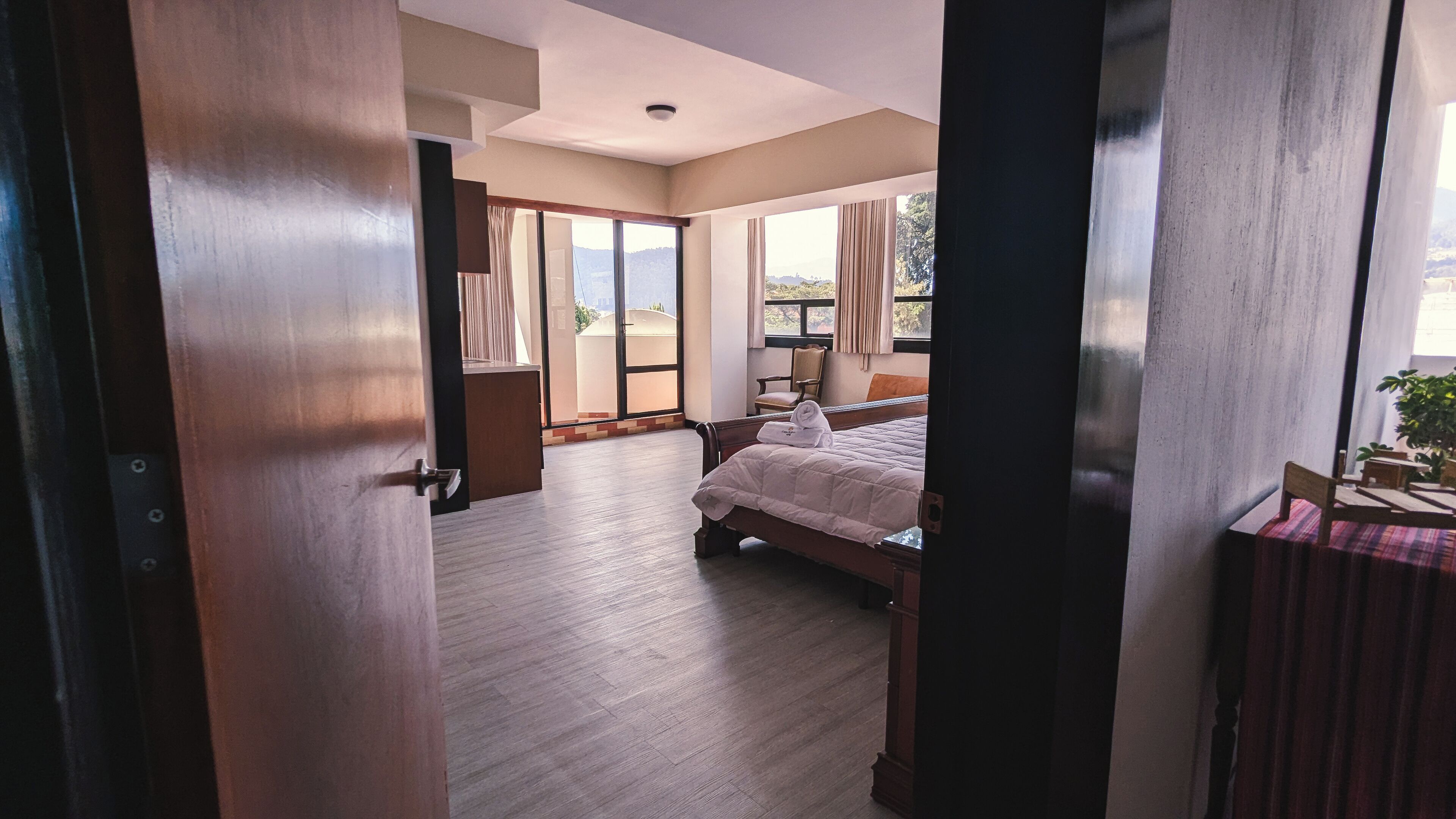 Quarto de hotel com cama, poltrona, mesa e vista para o exterior.
