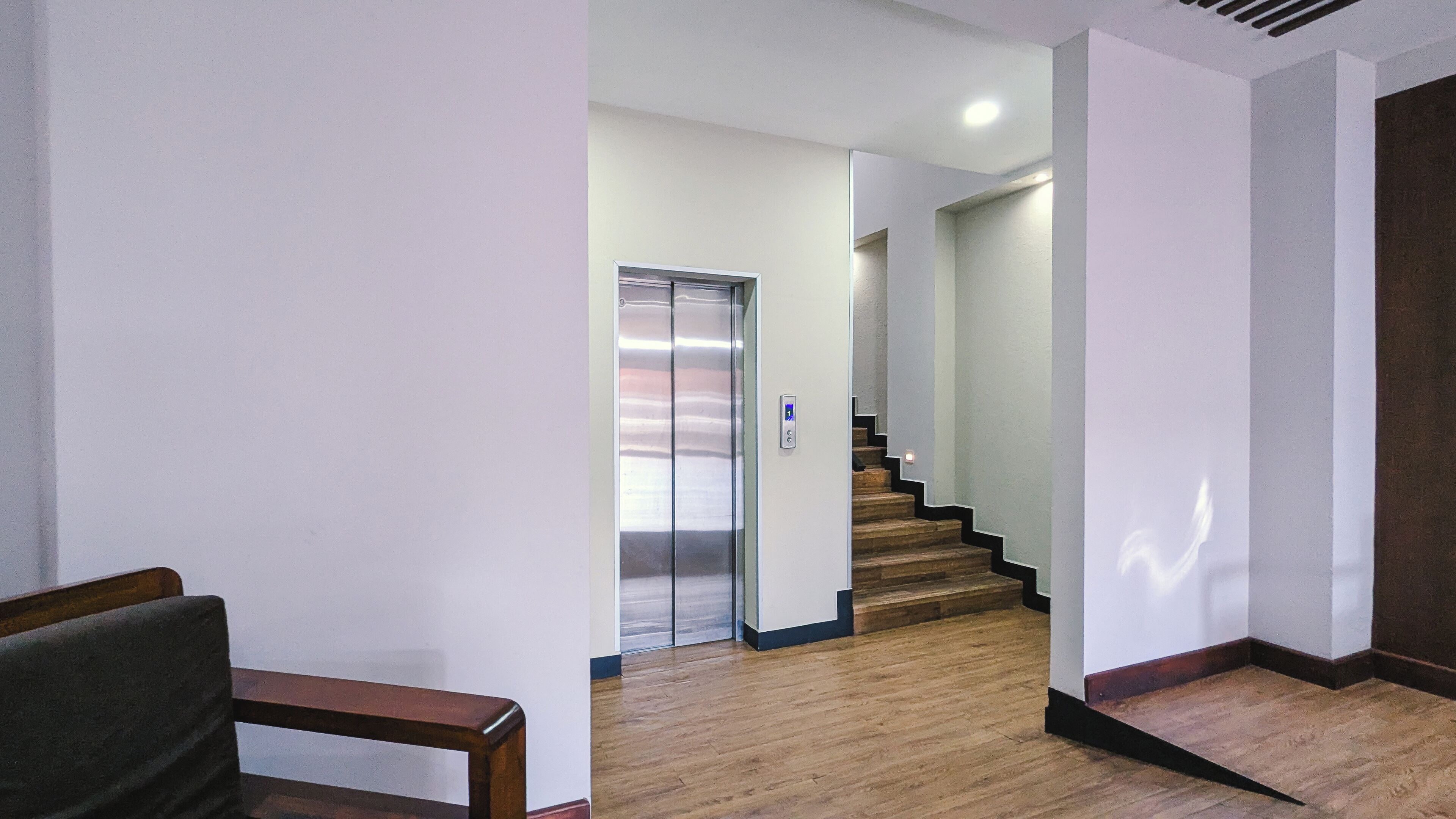 A hallway with a wooden floor, a staircase, and an elevator.