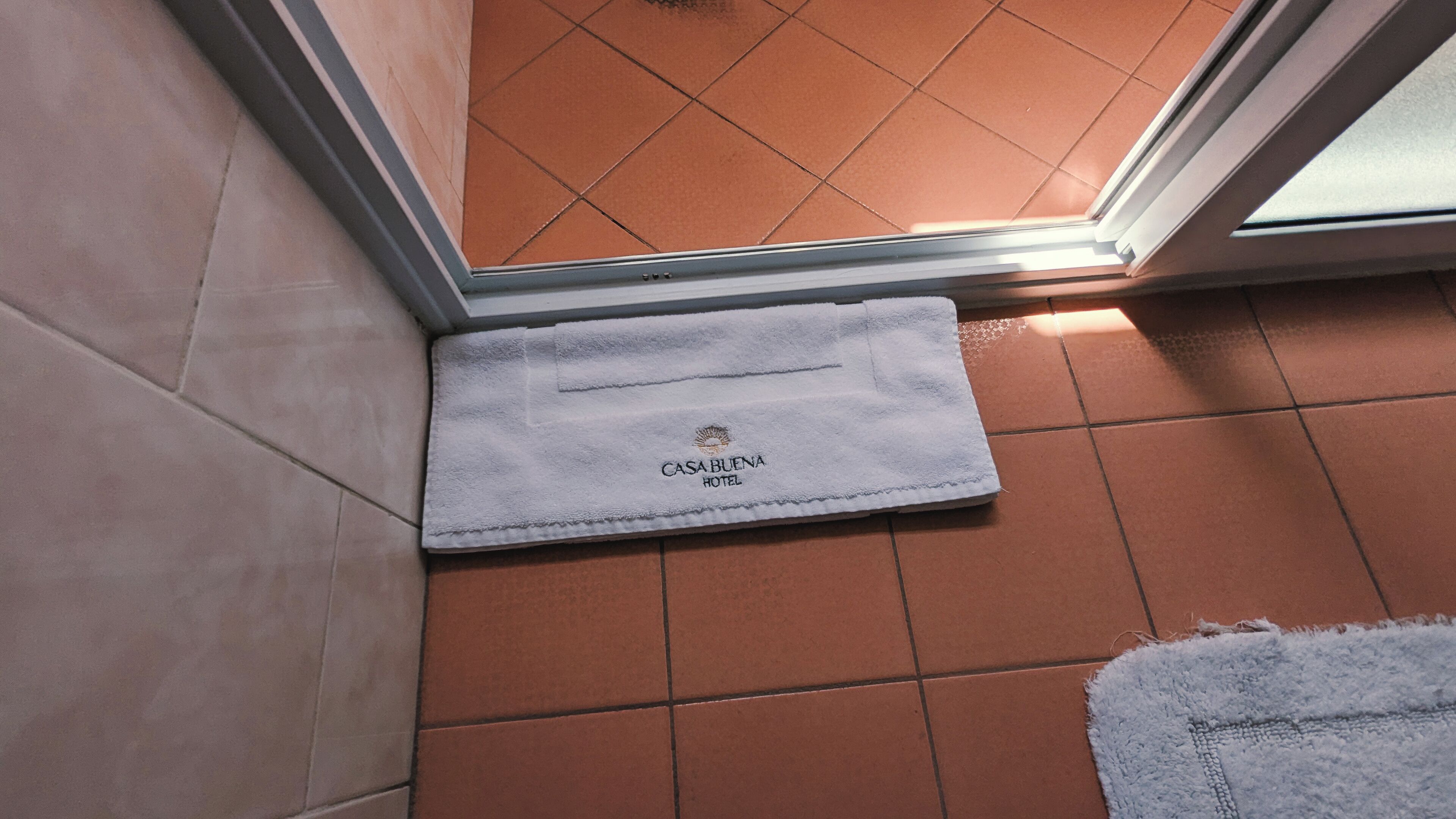 A white towel with "CASABUENA HOTEL" text on a tiled floor near a door.