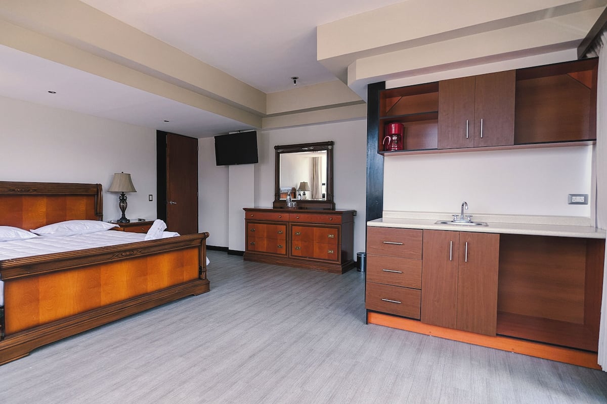 A hotel room with a wooden bed, a wooden dresser, a mirror, a TV, and a sink.