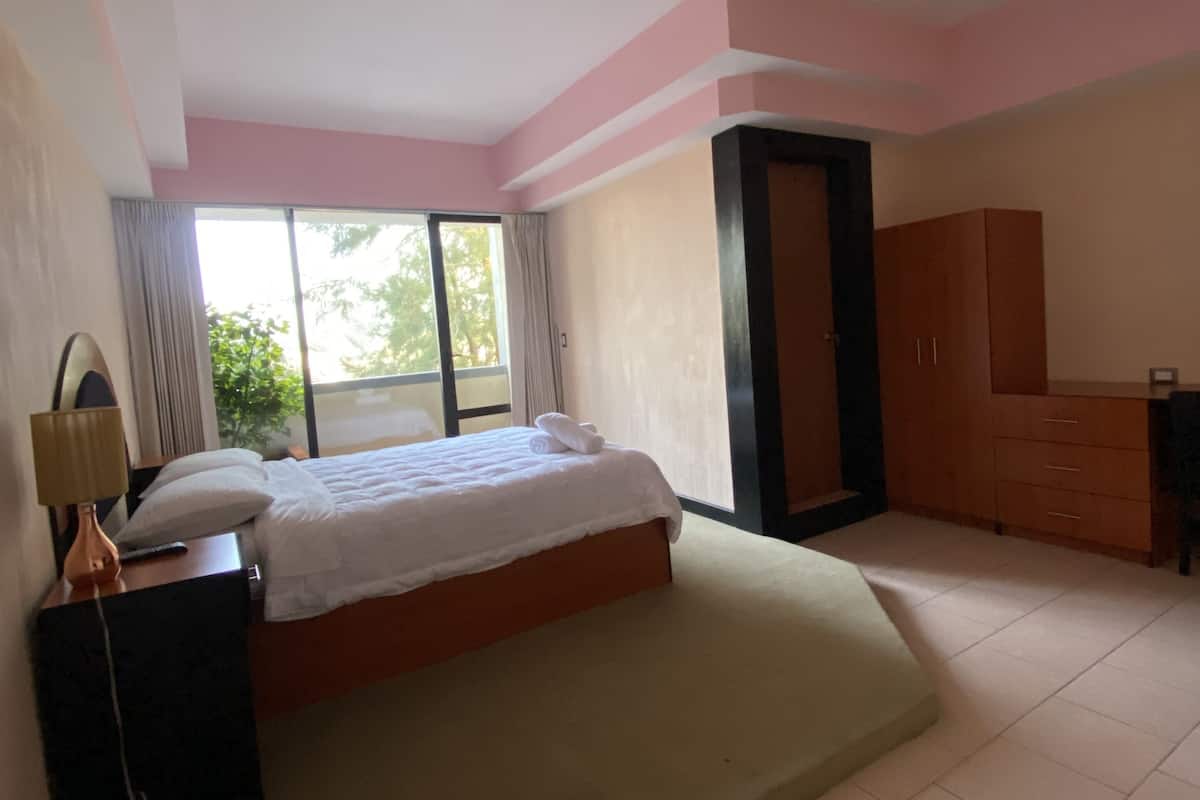 A bedroom with a bed, a dresser, a mirror, and a window.