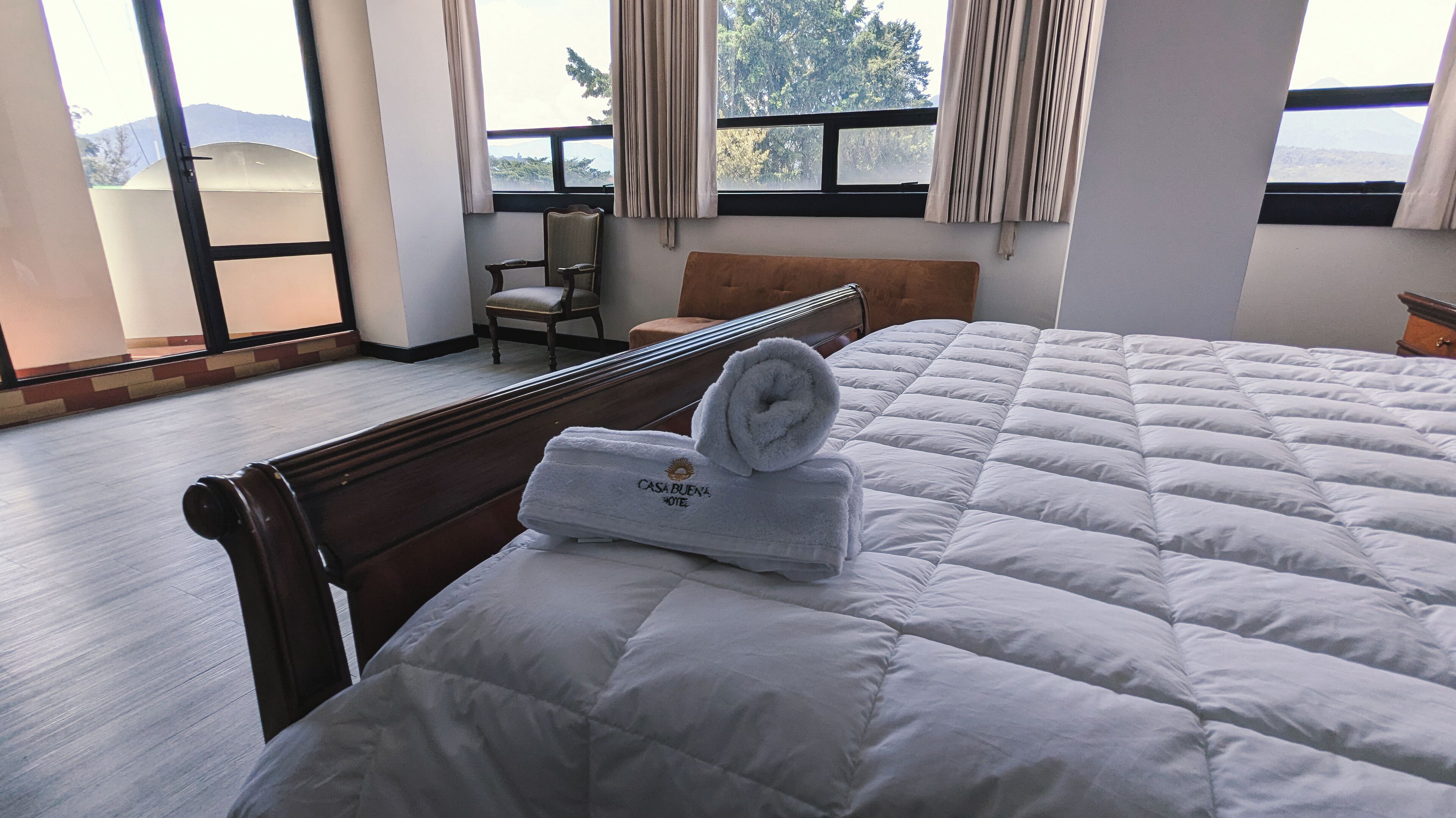 Habitación de hotel con una cama grande, un banco de madera, una silla y vistas al exterior a través de una ventana.