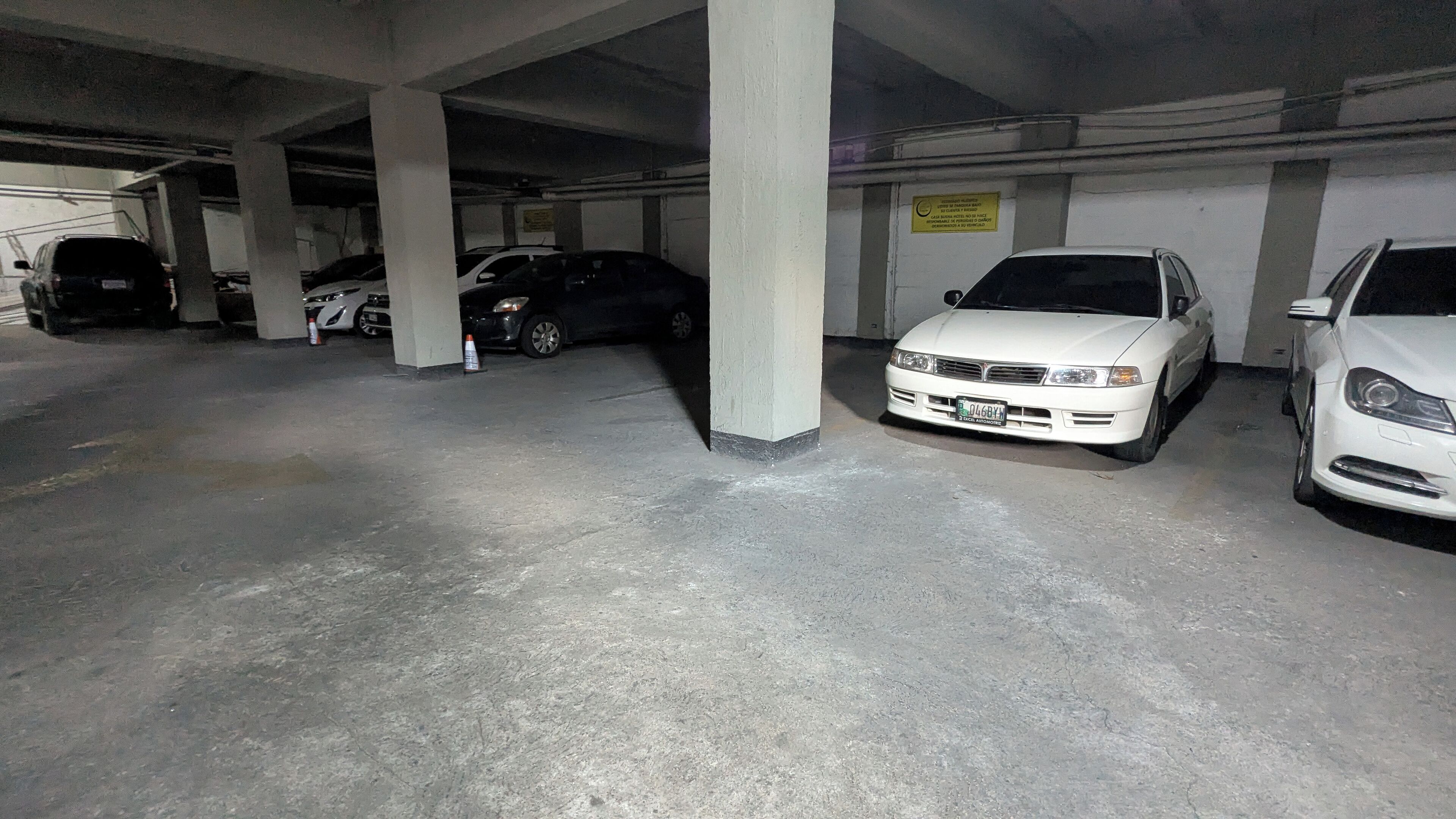 Un garaje para coches con pilares de hormigón y algunos vehículos estacionados.