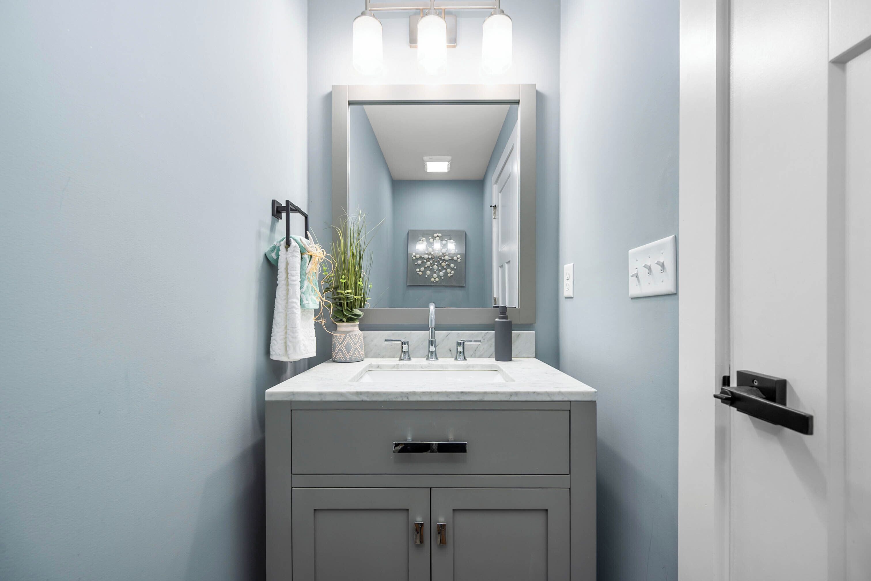 A bathroom with a white sink, grey cabinets, a large mirror, and a potted plant.