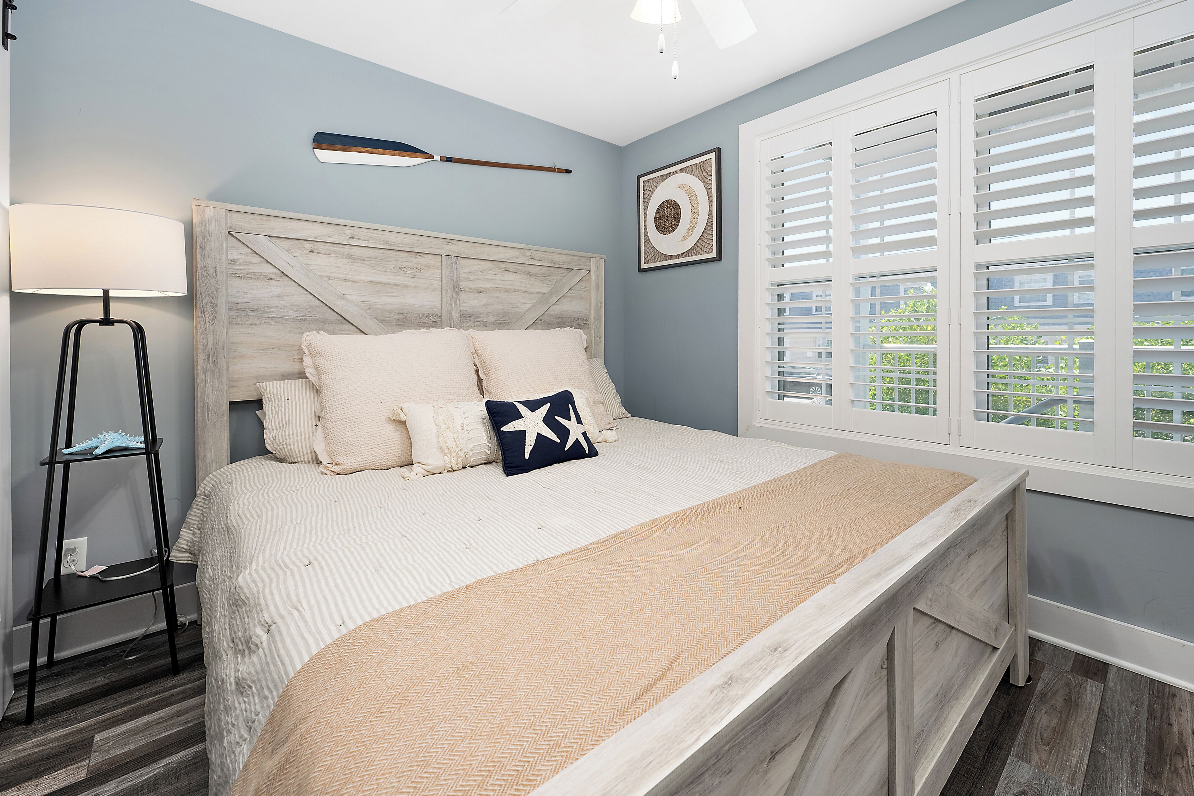 Quarto com cama, luminária de cabeceira, janela com persianas e um objeto decorativo na parede.