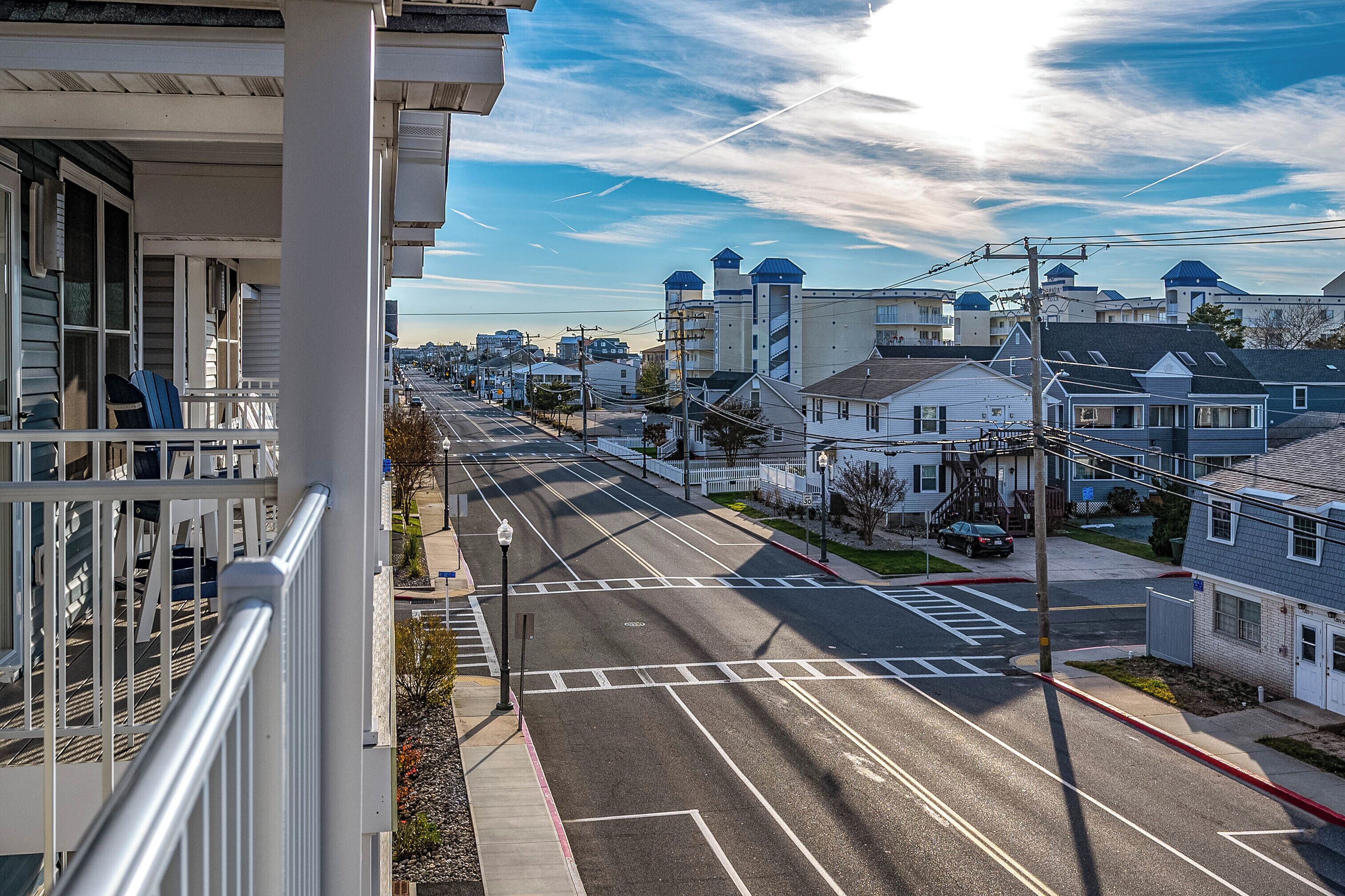 A residential street with houses, a clear sky, and a distant view of industrial buildings.