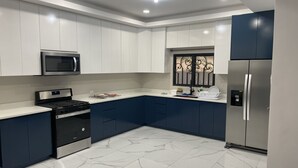 Una cocina moderna con armarios blancos y azul oscuro, electrodomésticos de acero inoxidable y piso de mármol.