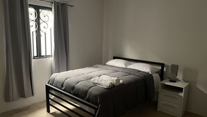 Un dormitorio con cama, cortinas, mesita de noche y ventana.