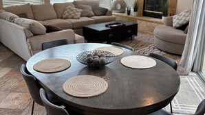 Een moderne woonkamer met een donkerhouten eettafel, omringd door stoelen, een beige bank en een aan de muur bevestigde televisie.