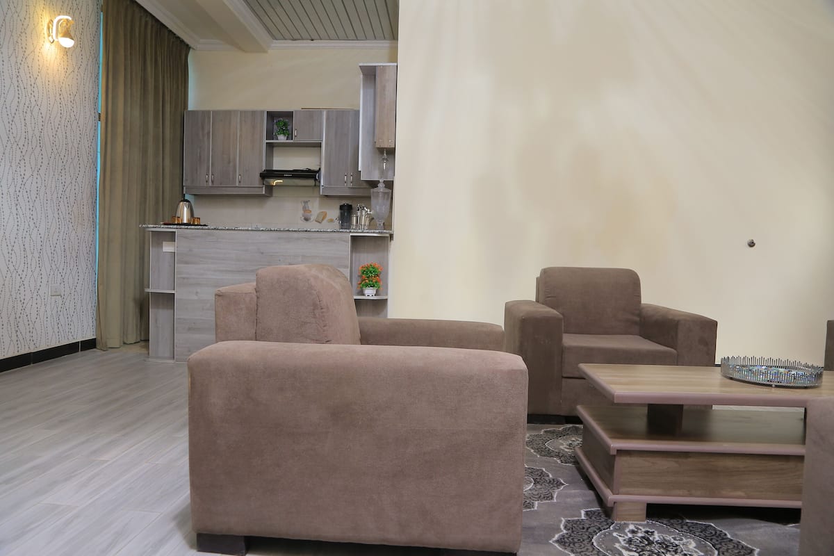 A modern living room with two beige sofas, a wooden coffee table, and a kitchen area in the background.