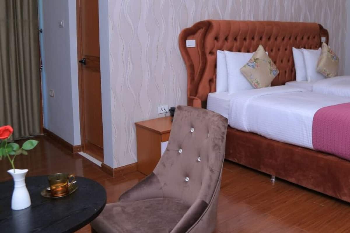 A hotel room with a large bed, a chair, a small table with a vase and a cup, and a door.