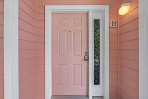 A pink door with a white frame, a glass door panel, and a light fixture above it.