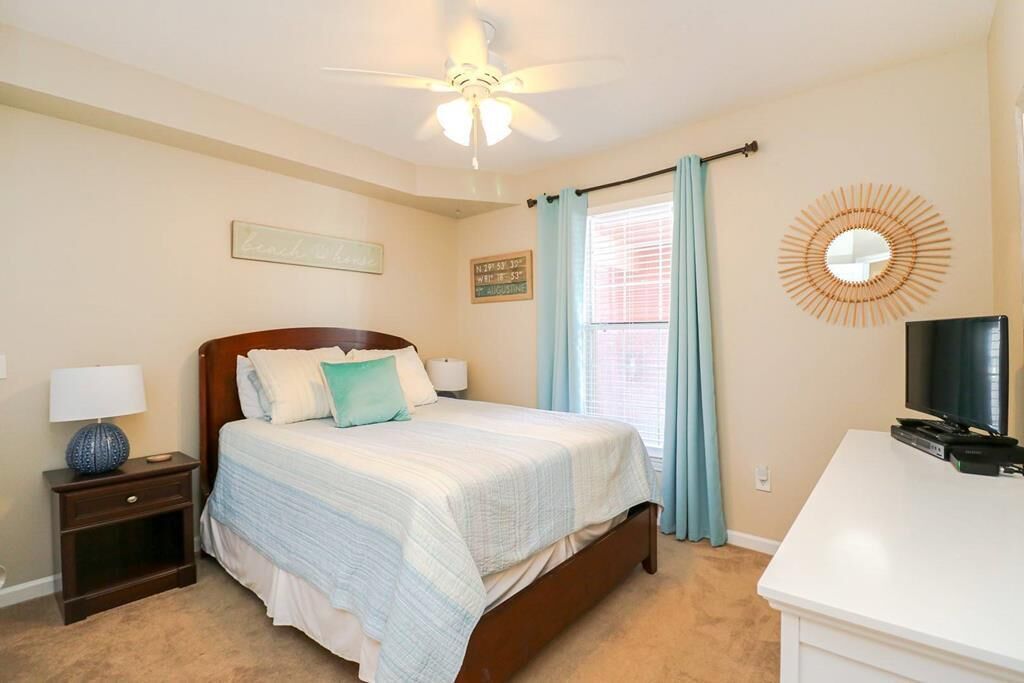 A bedroom with a bed, nightstand, TV, and a ceiling fan.