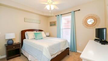 A bedroom with a bed, nightstand, TV, and a ceiling fan.