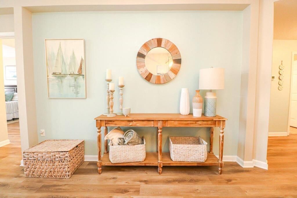 Una consola de madera con cestas de mimbre, un espejo y objetos decorativos frente a una pared clara.