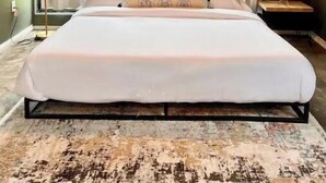 A large bed with a geometric light fixture above, a view of greenery outside, and a patterned rug on the floor. - Guest House | King Bed | Zen Retreat (Irving)