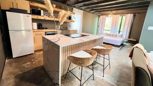 A modern kitchen with a marble island, bar stools, and a refrigerator. - Guest House | King Bed | Zen Retreat (Irving)
