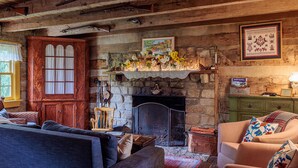 A rustic room with a fireplace, wooden furniture, and a stone wall. - Green Plains Cabin (South Charleston)
