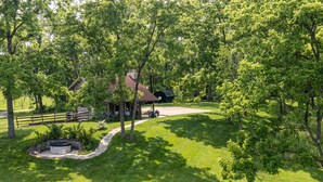 A rustic cabin with a stone fireplace, surrounded by lush greenery and a wooden fence. - Green Plains Cabin (South Charleston)