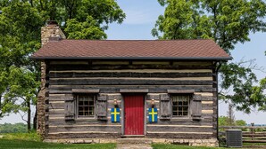 A log cabin with a red door, two windows with shutters, and a chimney. - Green Plains Cabin (South Charleston)