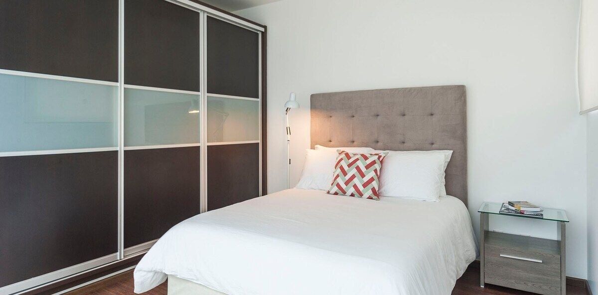 A modern bedroom with a large bed, a bedside table, and a wardrobe with sliding doors.