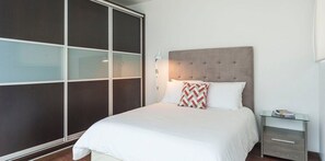 A modern bedroom with a large bed, a bedside table, and a wardrobe with sliding doors.