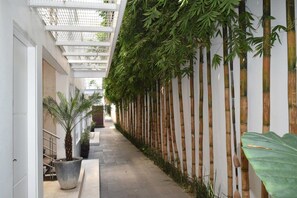 A corridor with a bamboo wall, a concrete floor, and a metal railing on the left.
