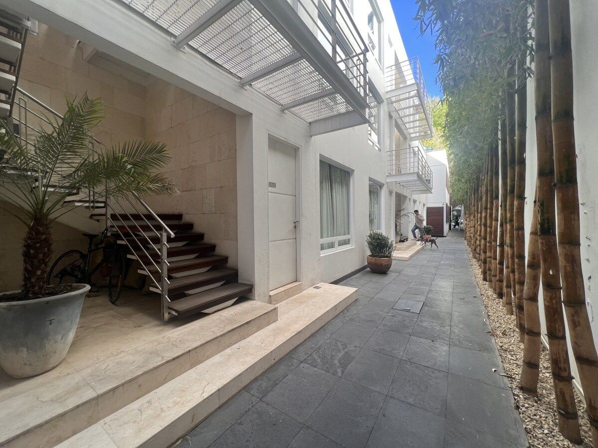 A narrow street with a building featuring a staircase, a bicycle, and potted plants.