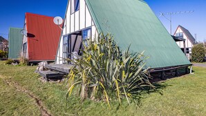 Une maison avec un toit en pente, une antenne parabolique et une grande plante dans le jardin.