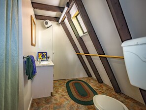 A small, narrow bathroom with a sloped ceiling, a toilet, a sink, and a shower area.
