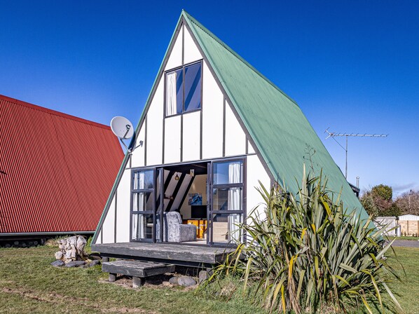 A small, triangular house with a green roof and white walls, featuring a large window and a satellite dish.